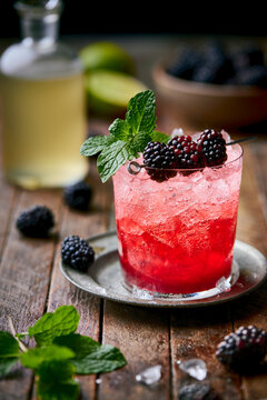 A vibrant Blackberry Smash cocktail sits in a rustic rocks glass filled with crushed ice, garnished with fresh blackberries