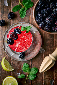 A vibrant Blackberry Smash cocktail sits in a rustic rocks glass filled with crushed ice, garnished with fresh blackberries