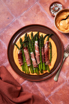 Asparagus with parma ham and aioli on plate with salt on toled background]
