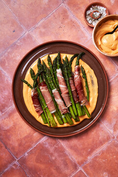 Asparagus with parma ham and aioli on plate with salt on toled background]
