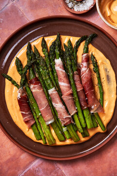 Asparagus with parma ham and aioli on plate with salt on toled background]