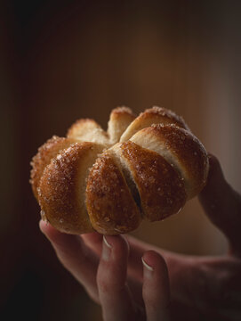A woman's hand holding a home baked pumpkin shaped sweet bun with a sugar coating