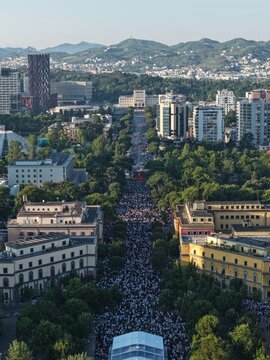 Tirane, Albania - 28 May 2026: Aerial view of a massive crowd gathered on a tree-lined boulevard surrounded by urban architecture and distant hills.