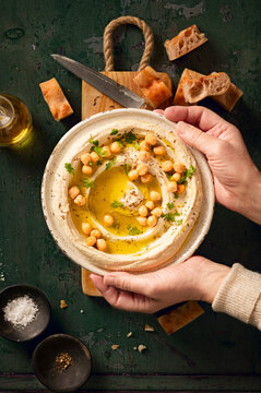 Hummus dip in ceramic plate with pita bread, hands holding the plate