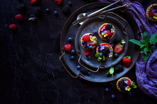 Lemon tarts with berries and viola edible flowers on dark background.