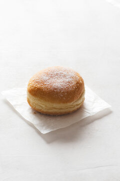 Krapfen, soft and golden, generously dusted with grains  sugar. Set against a light, luminous background to highlight its warm, inviting colors&mdash;ideal for Carnival or a indulgent snack