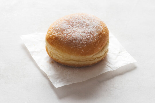 Krapfen, soft and golden, generously dusted with grains  sugar. Set against a light, luminous background to highlight its warm, inviting colors&mdash;ideal for Carnival or a indulgent snack