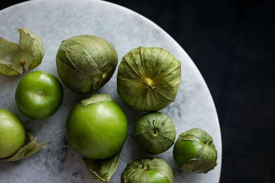 Fresh green tomatillos with husks on a marble surface