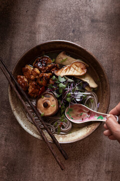 Spoon dipping into soup bowl of Vegan miso noodles with mushrooms, tempeh, and fresh microgreens