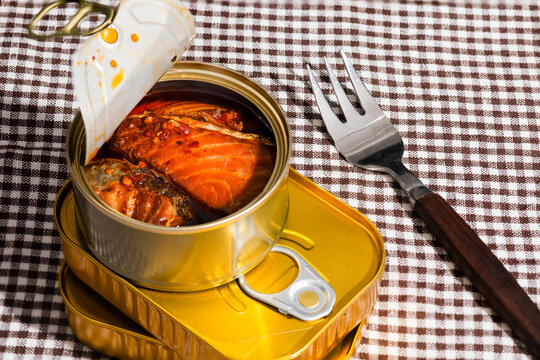 Opened tin of salmon in oil stacked on cans with fork on cloth