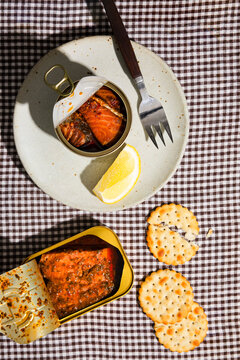 Flat lay of tinned fish with lemon, fork, and crackers in hard light