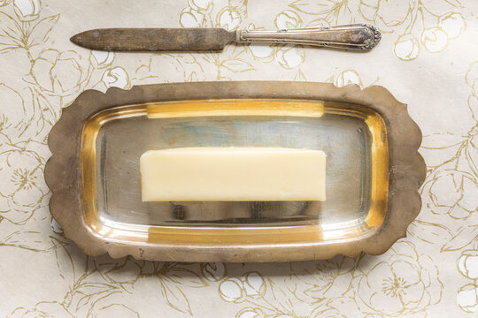 Block of butter on ornate silver tray with vintage knife above