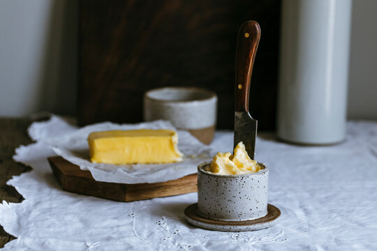 Rustic butter in ceramic jar with knife and block on table