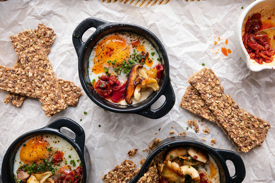 Baked eggs en cocotte with mushrooms, tomatoes, and seed crackers