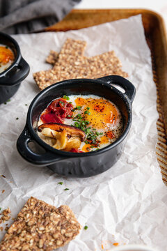 Baked eggs en cocotte with mushrooms, tomatoes, and seed crackers