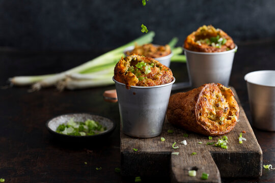 Cheddar scallion popovers in metal cups on rustic wooden board