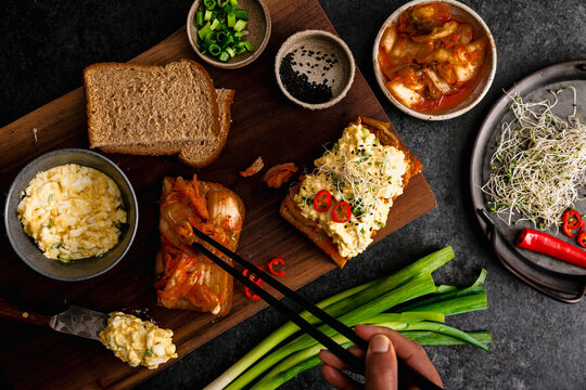 Chopsticks reaching for kimchi beside egg salad toast