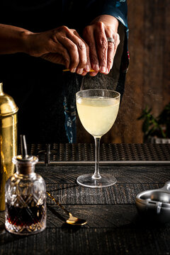 A hand squeezing a lemon over a cocktail