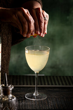 Bartender zesting citrus over a cocktail glass at a dim bar