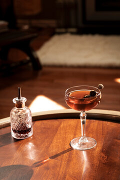 Coupe cocktail with garnish of olives on wooden table in warm sunlight