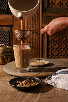 Masala chai being strained into a glass on a rustic wooden table