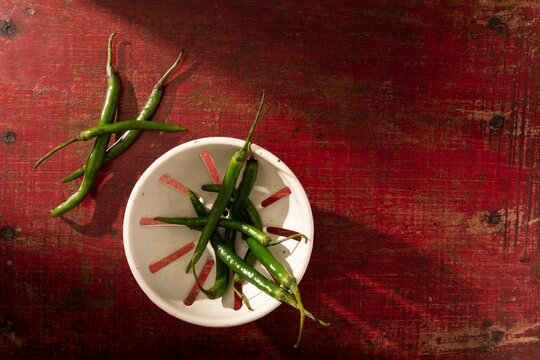 Fresh green chilies on a rustic red wooden surface