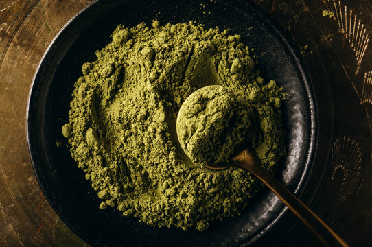 Close-up of matcha powder on a black plate with a gold spoon