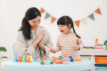 Naklejka premium Mother and daughter playing with colorful toy blocks in bright playroom, happy family moment