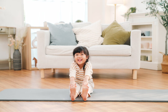 Child yoga, indoor exercise, home living, smiling girl, stretching pose, living room