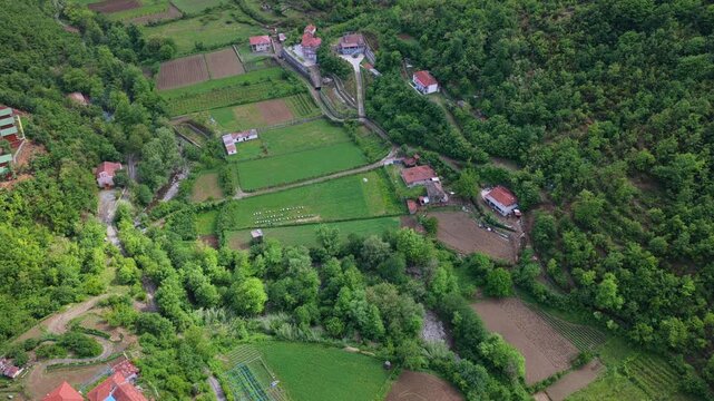 An overhead aerial video of rural homes, backyard gardens, and the dense forest edge of Katund i Vjeter village within the Mirdita Region of Albania.