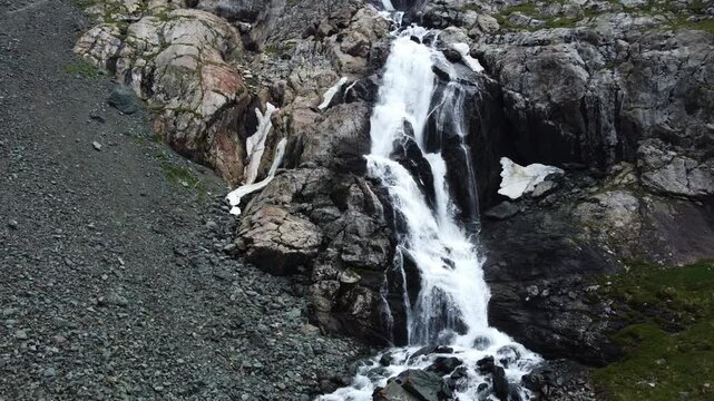 Close up aerial view of powerful mountain waterfall with melting snow patches on rocky cliffs, Ala-Kul, Kyrgyzstan, Karakol. High quality 4k footage
