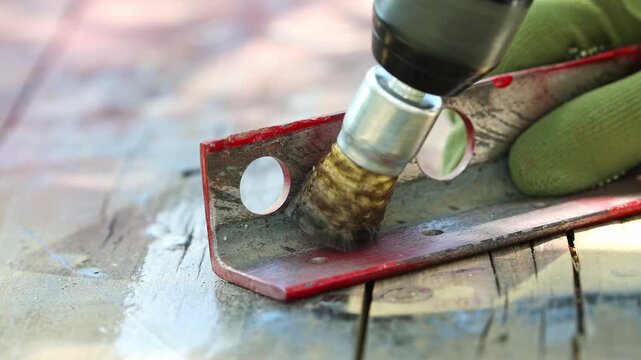 Worker hands in gloves holding drill tool with rotating abrasive steel brush, polish and clean rust on metal outdoor.