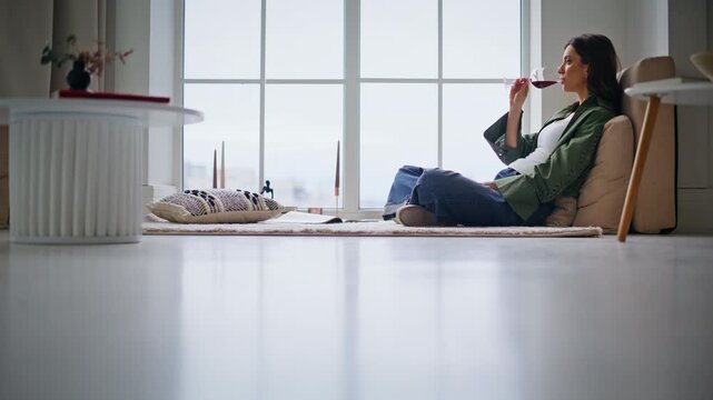 Single brunette sipping wine from glass goblet relaxing in light apartment alone