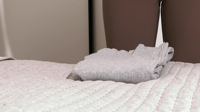 Hands fold knit clothes on a bed. A person stacks a sweater in a tidy home setting. Laundry care, packing, and organizing concept for lifestyle and housekeeping..