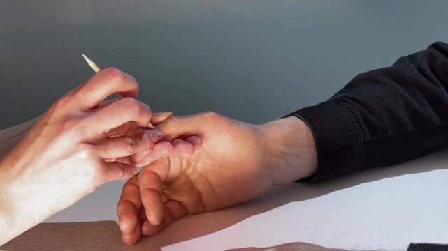 Manicure treatment in close up. Technician shapes nails with cuticle tool on a client hand. Salon beauty care for nail repair and grooming..