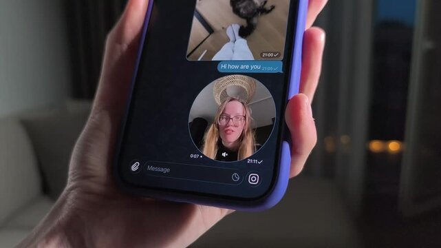 Hand holds smartphone with a chat video message on screen. The mobile interface shifts from still preview to active conversation. Social media communication and app mockup concept..