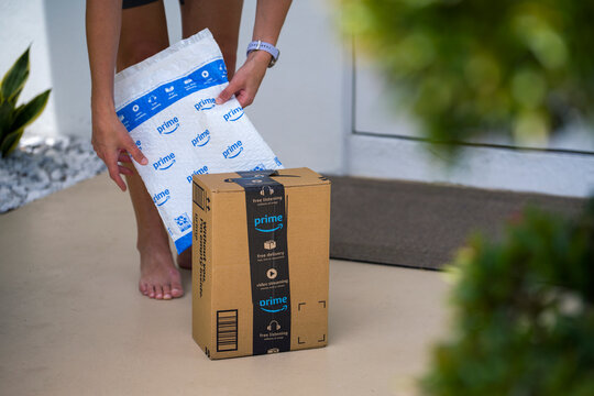 Close view of woman picking up delivered Amazon package at house entrance. Doorstep delivery and efficient online shopping service concept. Sarasota, USA - May 4, 2026.
