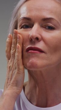 Close up portrait: old woman, taking face cream for older skin with fingertip. Advertising of antiwrinkle antiaging whitening rejuvenation uv protection senior female in menopause treatment. Wrinkles