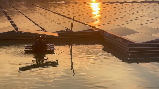Floating solar panels and solar-powered water aerator on a lake during a golden sunset, renewable green energy footage
