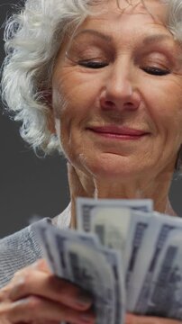 Portrait: Happy senior woman with grey hair counting USD banknotes. Rich old lady getting rich with jackpot. Face of mature female person holding cash money paper dollars. Wealth retirement concept