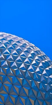Abstract close-up of a futuristic geodesic dome with metallic triangular patterns against a clear blue sky.