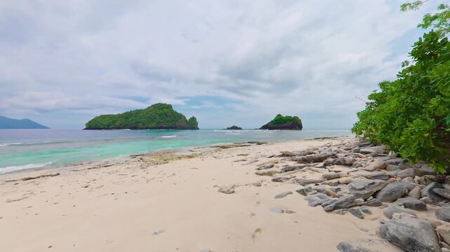 Static shot of a pristine deserted white sand beach on Masare Island, Sitaro Regency, North Sulawesi, Indonesia, featuring crystal clear turquoise ocean water and tropical greenery.