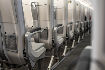 Fototapeta premium Modern airplane cabin interior with ergonomic grey economy class seats, foldable tray tables, mesh storage pockets and metal supports, soft ambient lighting, clean minimal design.