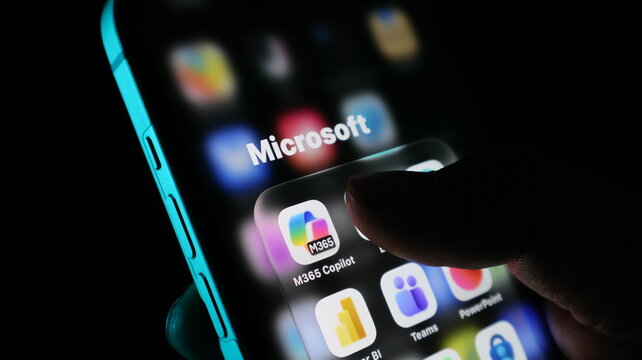 Closeup of a person using a smartphone with microsoft 365 copilot app icon visible on the screen in a dark environment