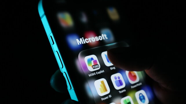 Closeup of a smartphone screen displaying microsoft application icons including m365 copilot, bing, power bi, teams, and powerpoint
