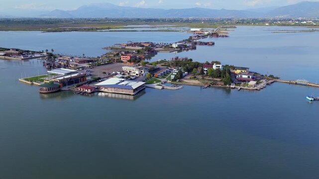 Aerial video featuring  waterfront hotels, restaurants, parking lots, and wooden fishing cabins along the Patok Lagoon in Albania.