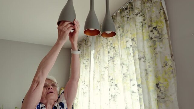 Senior woman installing light bulb into hanging lamp
