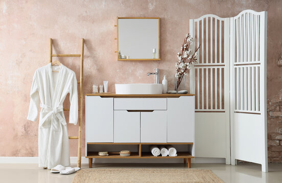 Interior of bathroom with sink, folding screen and bathrobe on ladder