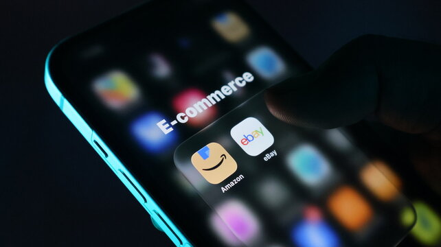 Closeup of a persons finger touching an ecommerce folder on a smartphone screen, displaying amazon and ebay app icons