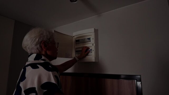 Senior Woman Checking Electrical Fuse Box at Home 